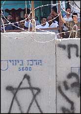 Palestinians are visible through the barbed wire, on the other side of the wall, waiting to pass through the checkpoint to the other side.