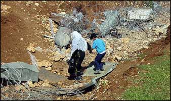 A mother and child on their way home take a route bypassing the checkpoint, through a temporary breach in the roll of barbed wire crossing their right-of-way.
