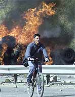 A Bolivian on a bicycle rides past burning cars during one of the recent anti-government riots in the capital.