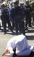 Prevented by Israeli occupiers from gaining access to the mosque, a devout Palestinian Muslim prays in public, ignoring laughter from brutal racist soldiers.